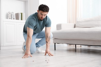 Photo of Emotional young man looking in disgust at cockroaches on floor indoors, space for text. Pest problem