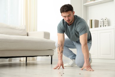 Photo of Emotional young man looking in disgust at cockroaches on floor indoors, space for text. Pest problem