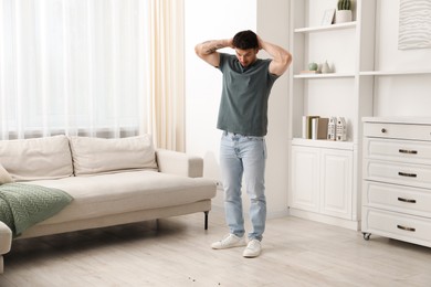 Photo of Emotional young man looking in disgust at cockroaches on floor indoors. Pest problem