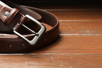 Photo of One brown leather belt on wooden table, closeup. Space for text