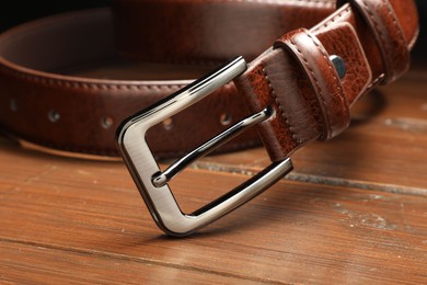 Photo of One brown leather belt on wooden table, closeup