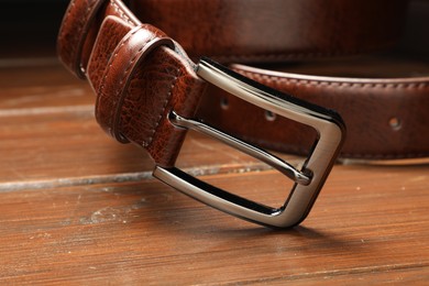 Photo of One brown leather belt on wooden table, closeup