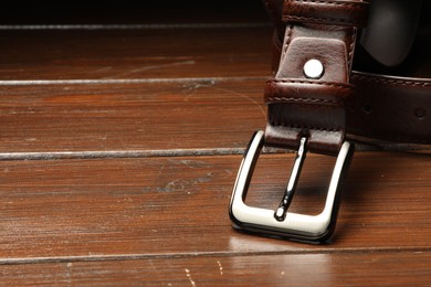 Photo of One brown leather belt on wooden table, closeup. Space for text