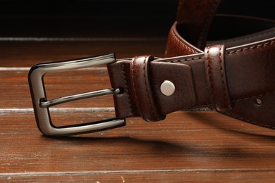 Photo of One brown leather belt on wooden table, closeup