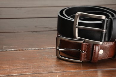 Photo of Two leather belts on wooden table, closeup. Space for text