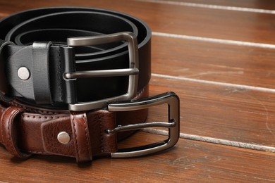 Photo of Two leather belts on wooden table, closeup. Space for text