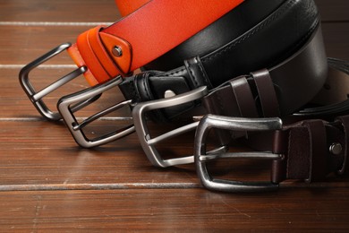Photo of Many leather belts on wooden table, closeup