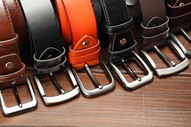 Photo of Many leather belts on wooden table, closeup
