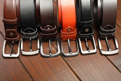 Photo of Many leather belts on wooden table, above view