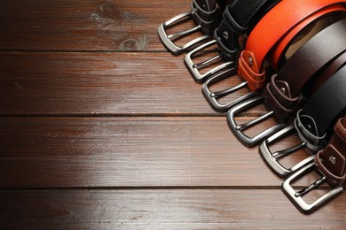 Photo of Many leather belts on wooden table, above view. Space for text