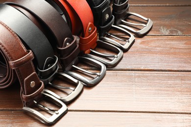 Photo of Many leather belts on wooden table, closeup. Space for text