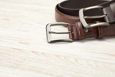Photo of Two brown leather belts on wooden table, closeup. Space for text