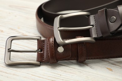 Photo of Two brown leather belts on wooden table, closeup