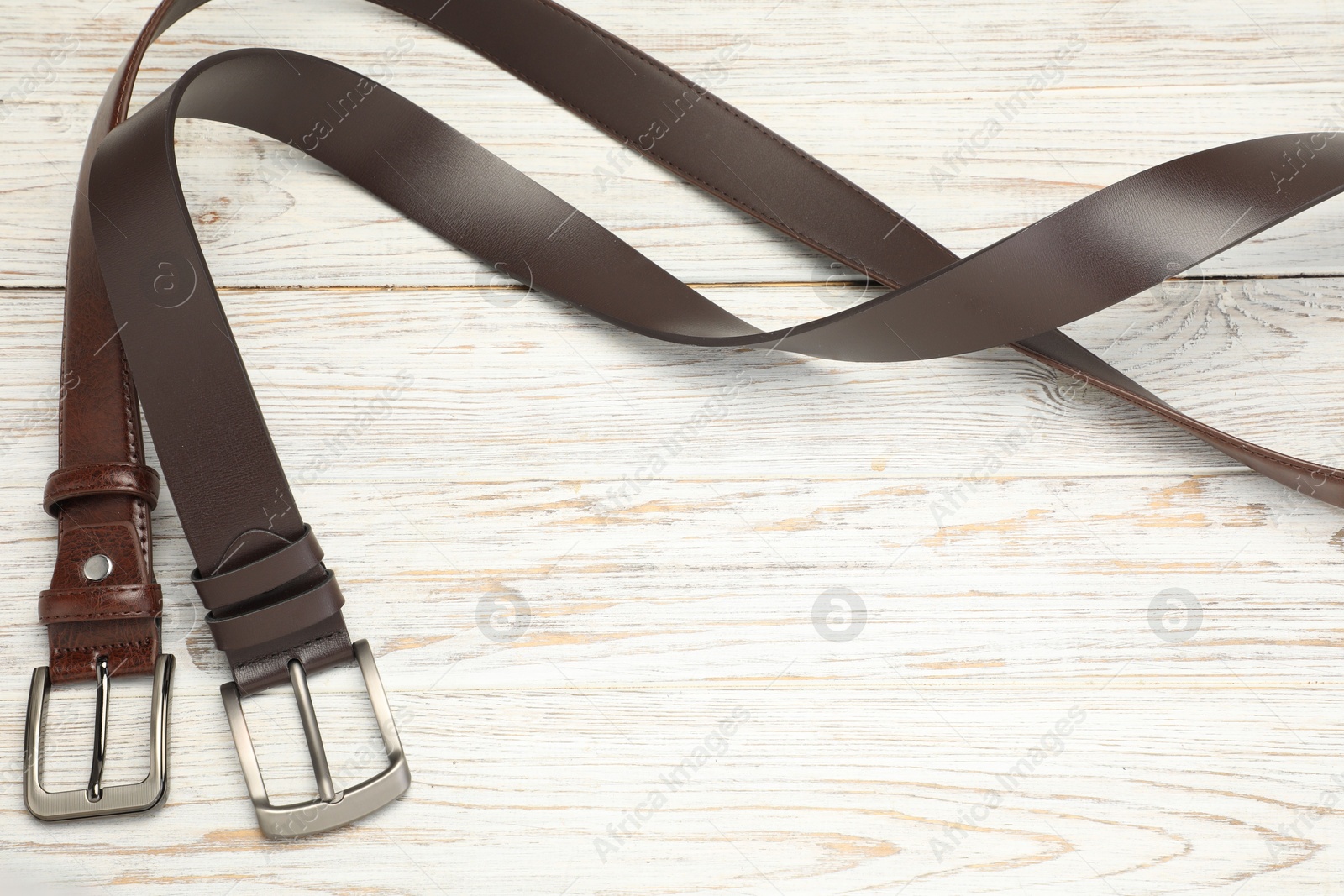 Two brown leather belts on wooden table, above view. Space for text Photo of Two brown leather belts on wooden table, above view. Space for text