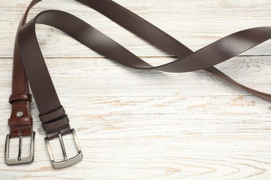 Photo of Two brown leather belts on wooden table, above view. Space for text