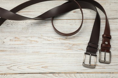 Photo of Two brown leather belts on wooden table, above view. Space for text