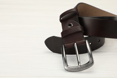 Photo of One brown leather belt on white wooden table, closeup. Space for text