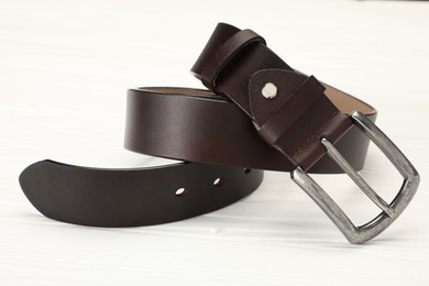 Photo of One brown leather belt on white wooden table, closeup