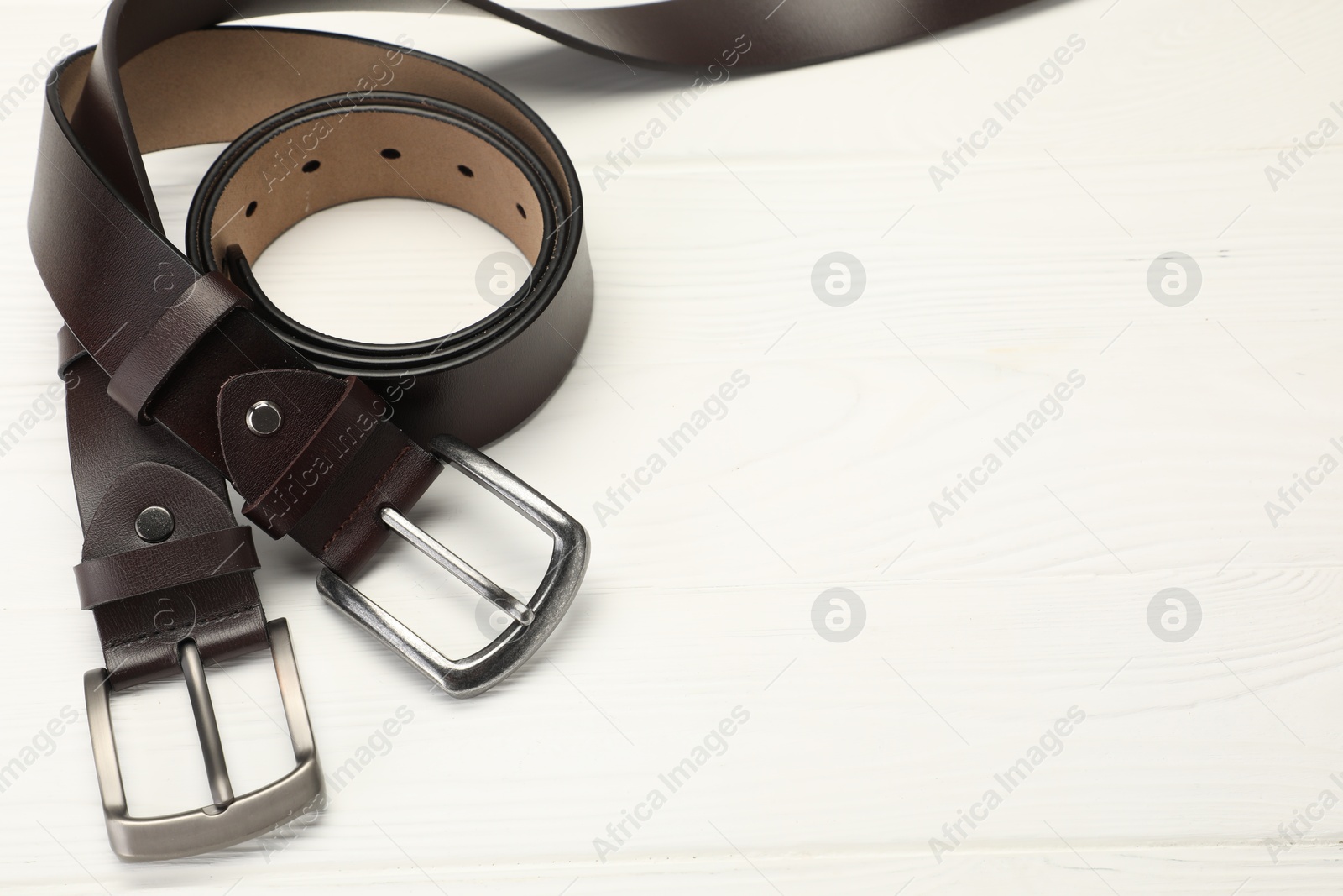 Two brown leather belts on white wooden table, above view. Space for text Photo of Two brown leather belts on white wooden table, above view. Space for text