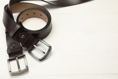 Photo of Two brown leather belts on white wooden table, above view. Space for text