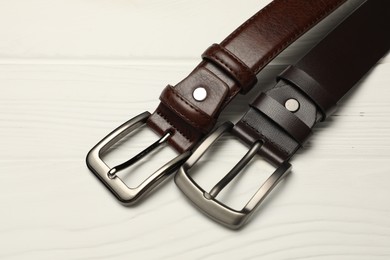 Photo of Two brown leather belts on white wooden table, above view