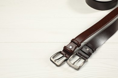 Photo of Two brown leather belts on white wooden table, above view. Space for text