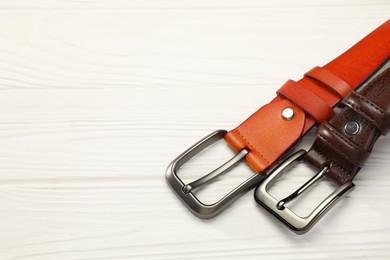 Photo of Two leather belts on white wooden table, above view. Space for text