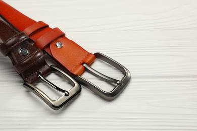 Photo of Two leather belts on white wooden table, closeup. Space for text