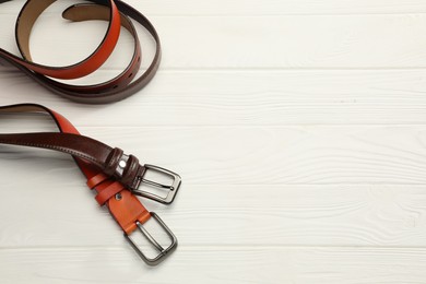 Photo of Two leather belts on white wooden table, above view. Space for text