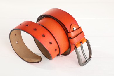 Photo of One orange leather belt on white wooden table, closeup