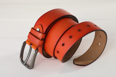 Photo of One orange leather belt on white wooden table, closeup