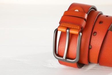 Photo of One orange leather belt on white wooden table, closeup. Space for text