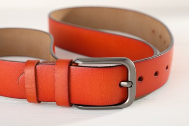 Photo of One orange leather belt on white wooden table, closeup