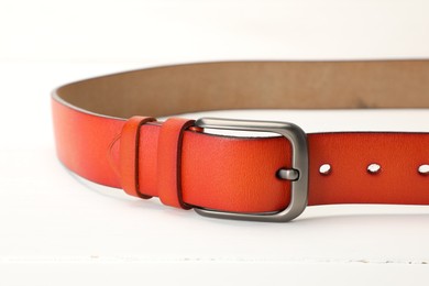 Photo of One orange leather belt on white table, closeup