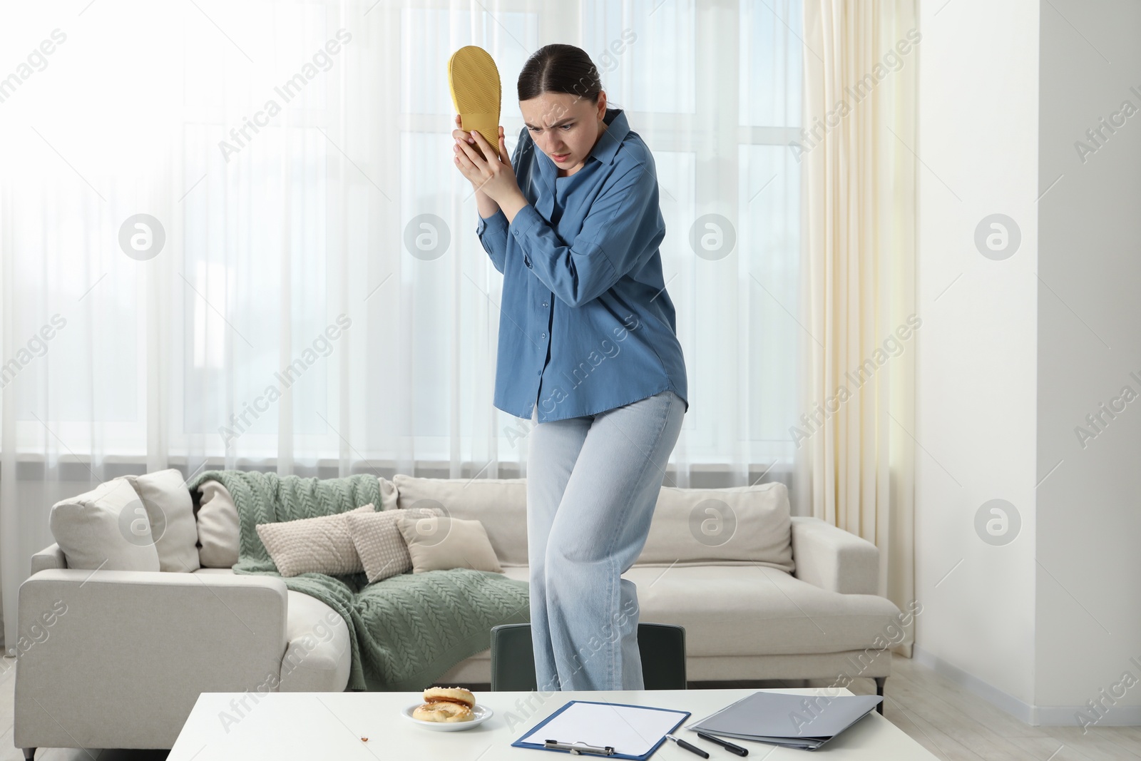 Photo of Young woman with slipper looking in disgust at cockroaches on white table indoors. Pest problem