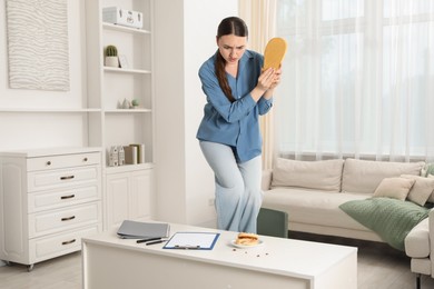 Photo of Young woman with slipper looking in disgust at cockroaches on white table indoors. Pest problem