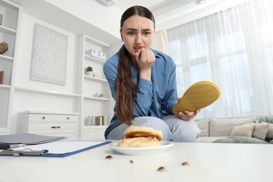 Photo of Young woman killing cockroaches with slipper on white table indoors, low angle view. Pest problem