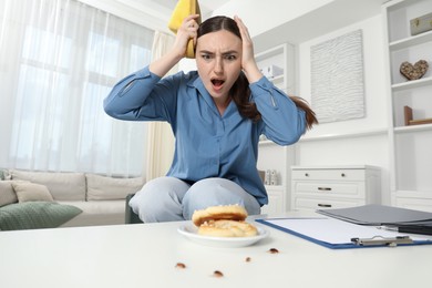 Photo of Young woman looking in disgust at cockroaches on white table indoors, low angle view. Pest problem