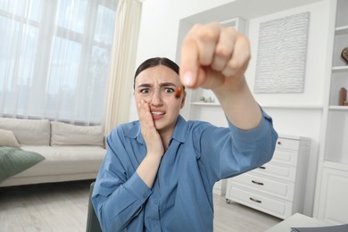 Photo of Shocked young woman holding cockroach indoors. Pest problem