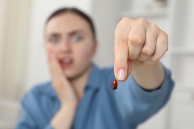 Photo of Shocked young woman holding cockroach indoors, selective focus. Pest problem