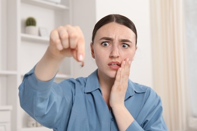 Photo of Shocked young woman holding cockroach indoors. Pest problem