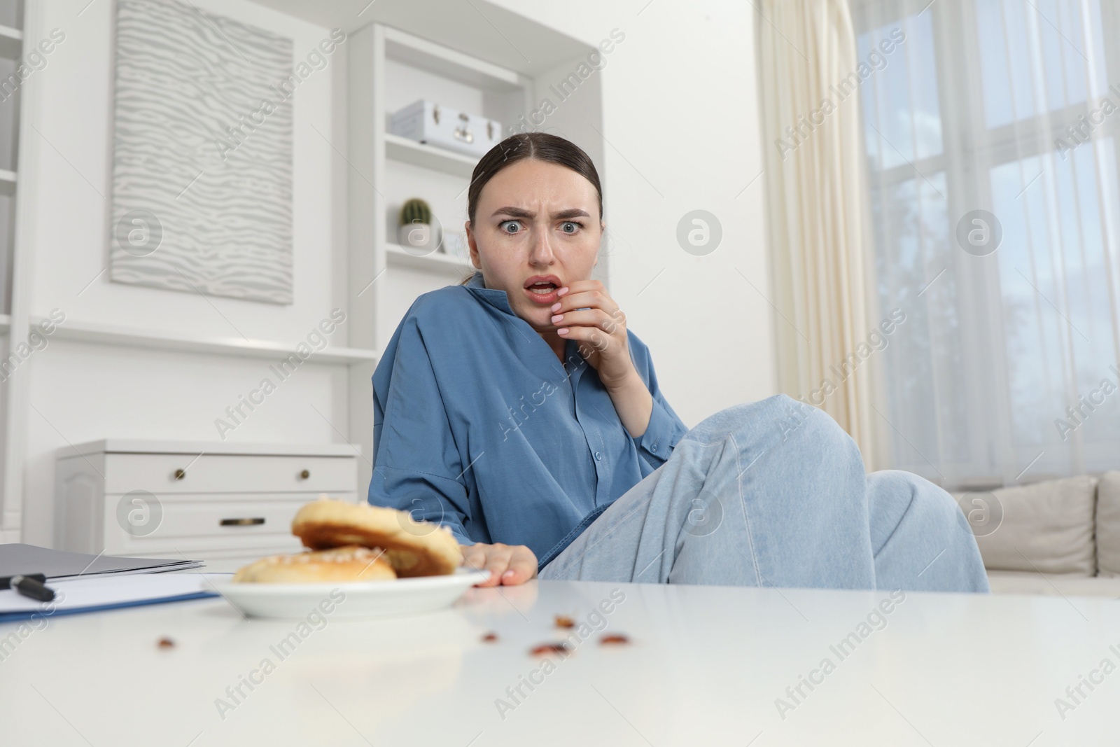 Photo of Shocked young woman looking at cockroaches and pretzels on white table indoors. Pest problem