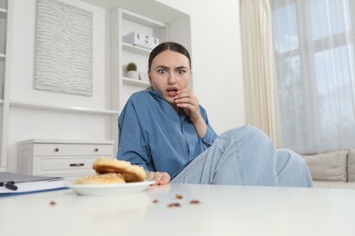 Photo of Shocked young woman looking at cockroaches and pretzels on white table indoors. Pest problem