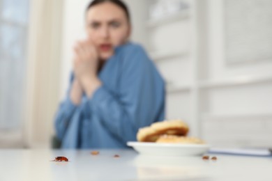 Photo of Shocked young woman looking at cockroaches and pretzels on white table indoors, selective focus. Pest problem