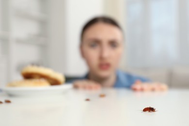 Photo of Shocked young woman looking at cockroaches on white table indoors, selective focus. Pest problem