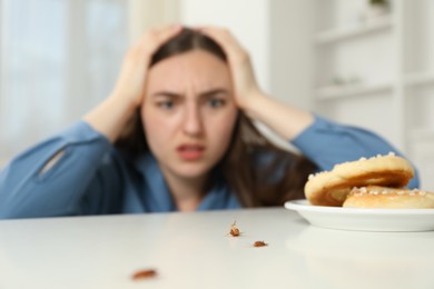 Photo of Shocked young woman looking at cockroaches and pretzels on white table indoors, selective focus. Pest problem