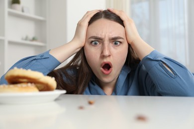 Photo of Shocked young woman looking at cockroaches and pretzels on white table indoors. Pest problem