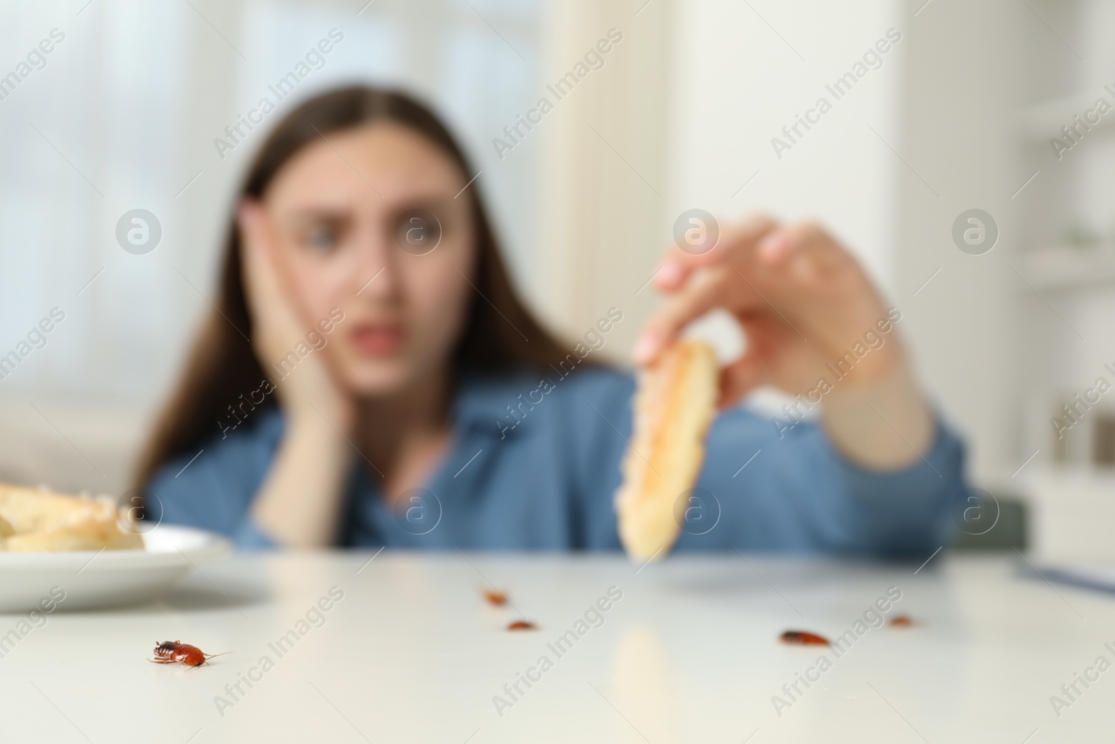 Shocked young woman holding pretzel with cockroach at white table indoors, selective focus. Pest problem Photo of Shocked young woman holding pretzel with cockroach at white table indoors, selective focus. Pest problem