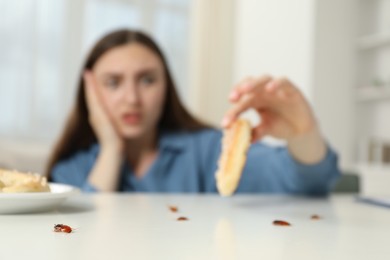 Photo of Shocked young woman holding pretzel with cockroach at white table indoors, selective focus. Pest problem