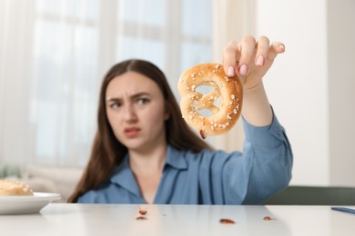 Photo of Shocked young woman holding pretzel with cockroach at white table indoors, selective focus. Pest problem